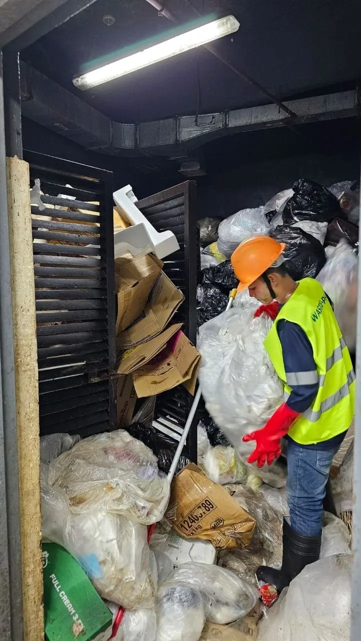 a man in a yellow vest and orange gloves holding a large bag of garbage